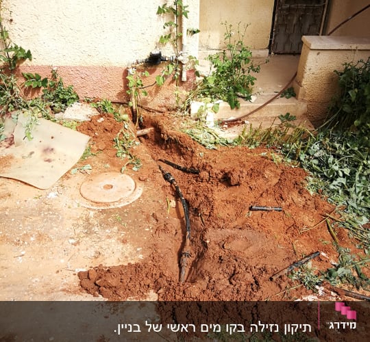 צינור מים חשוף באדמה ליד קיר חיצוני של מבנה